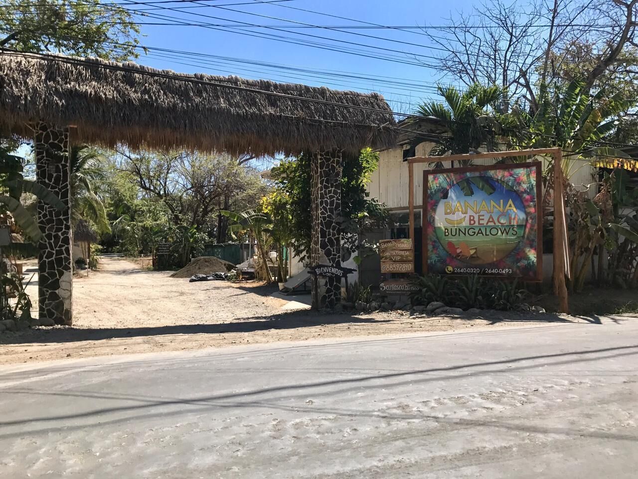 Una estructura con techo de paja, un letrero de Banana Beach Bungalows y un sendero de tierra que conduce a un edificio.