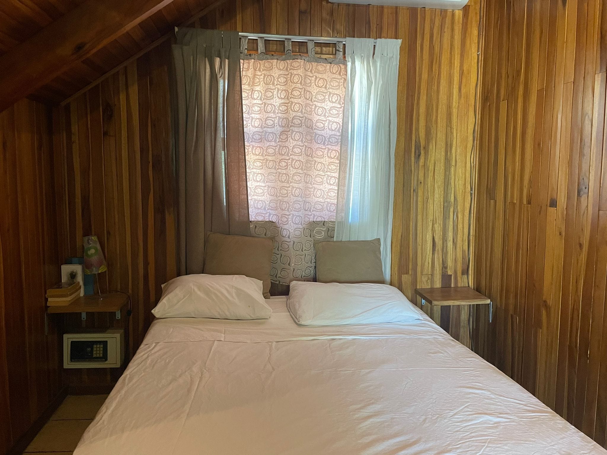 A wooden room with a bed, curtains, and a small table with a lamp.