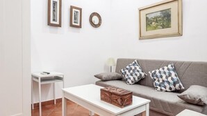 A living room with a grey sofa, patterned cushions, a white coffee table, and framed artwork on the wall. - HOUSE OF LIGHT apt 1 -Elegant Old Town 3PX wifi tv ac (Sevilla)