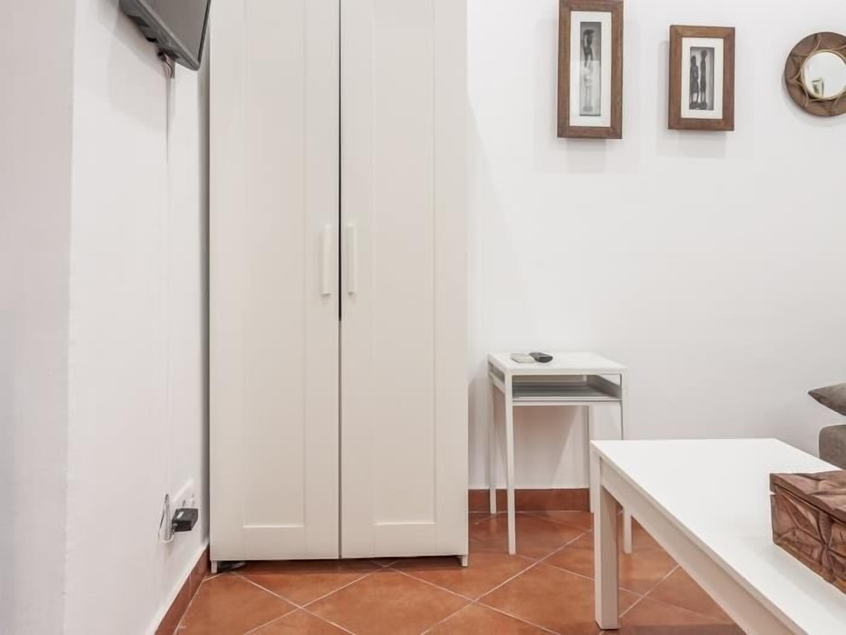 Une pièce avec une armoire blanche, une petite table blanche et un banc blanc. Deux tableaux encadrés sont accrochés au mur.
