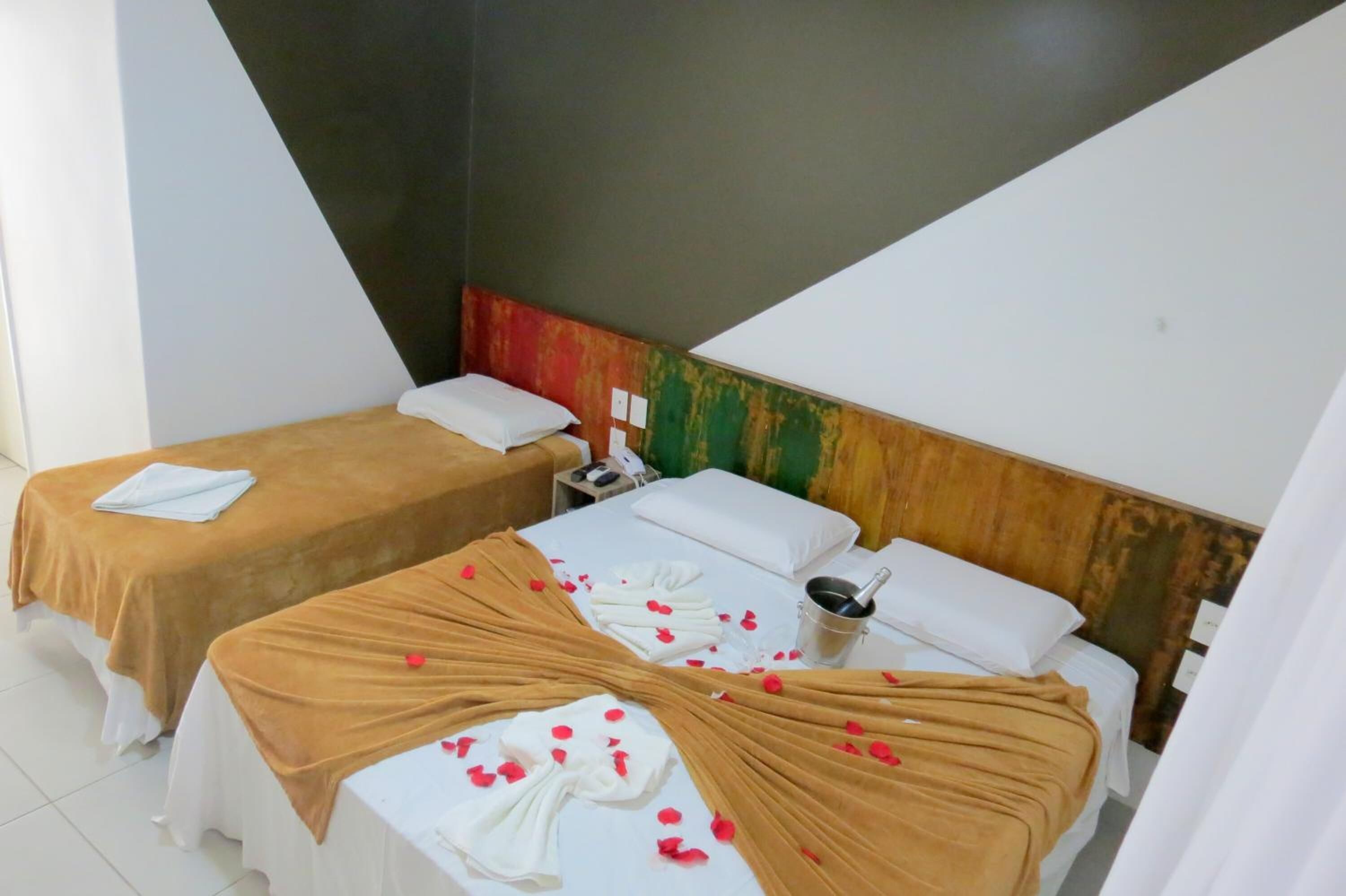 A hotel room with two beds, each with a brown bedspread and white pillows. There are rose petals on the beds, and a small table with a phone and a cup.