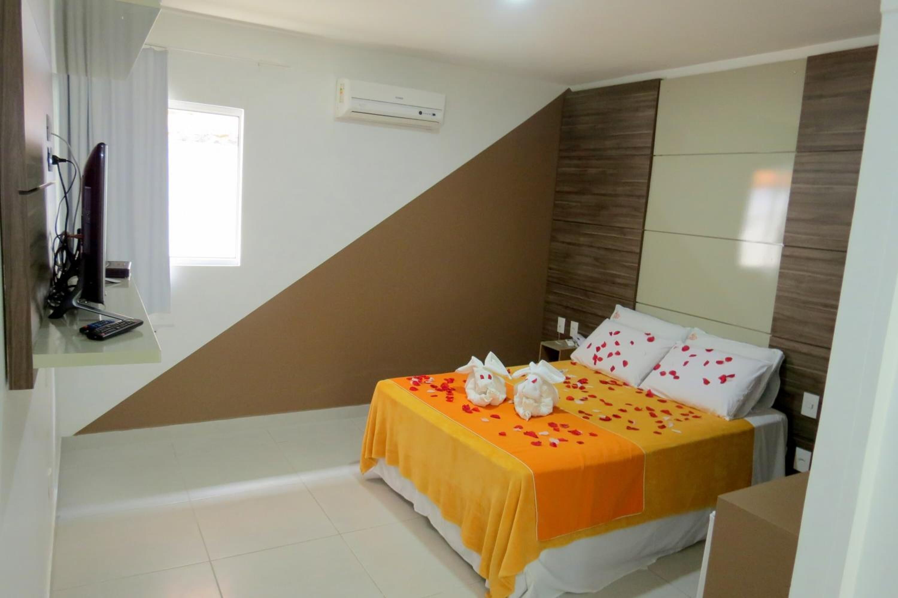 A hotel room with a bed, a nightstand, an air conditioning unit, a window with curtains, and a partial view of a bathroom.