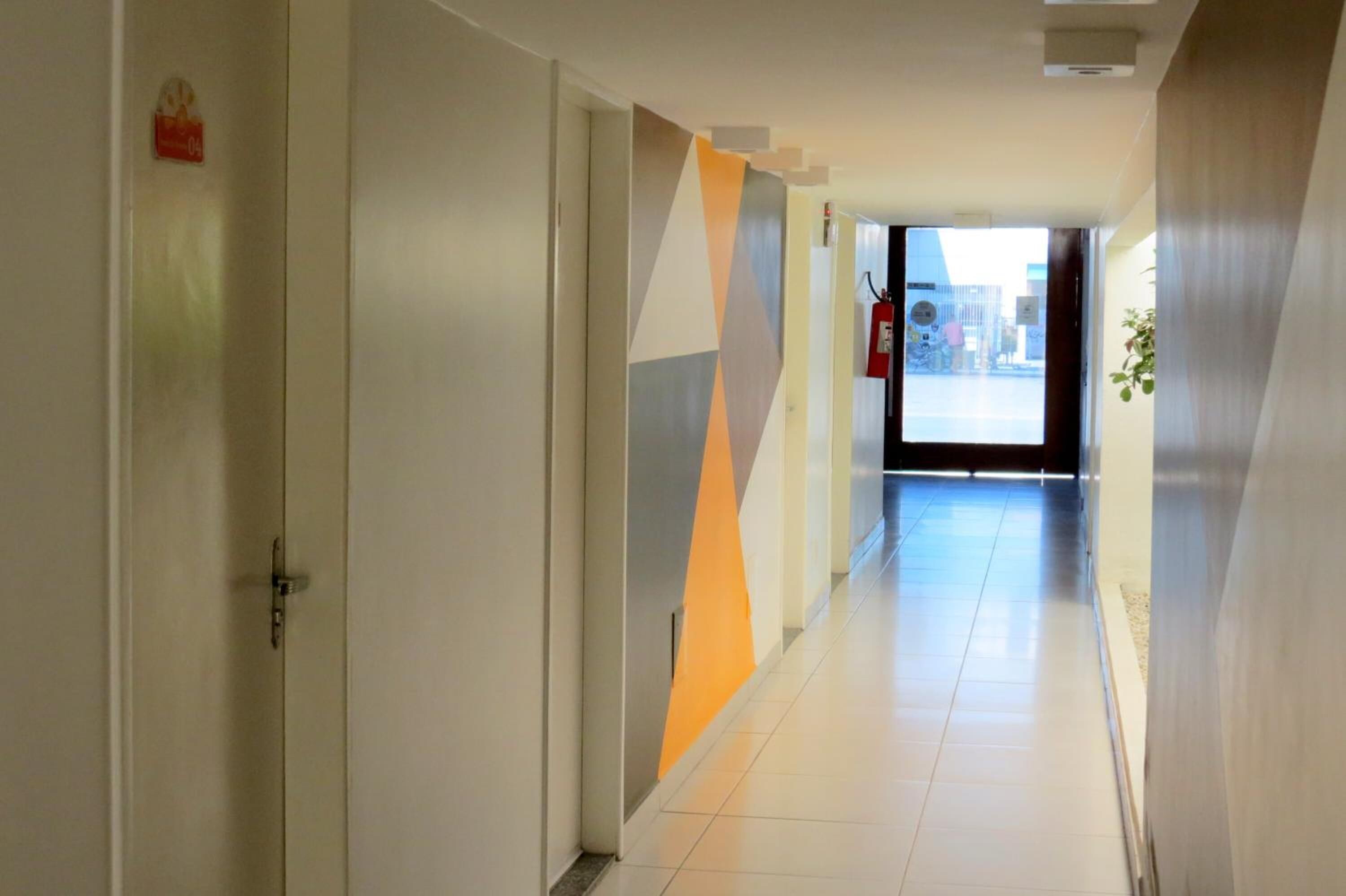 Un pasillo moderno con un diseño geométrico en la pared, un extintor y una puerta a la izquierda.
