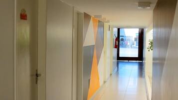 Un pasillo moderno con un diseño geométrico en la pared, un extintor y una puerta a la izquierda.