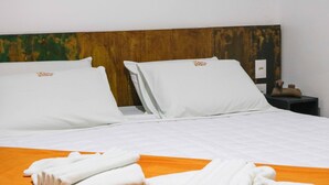 A hotel room with a neatly made bed, two pillows, an orange bedspread, and a folded towel on the bed.