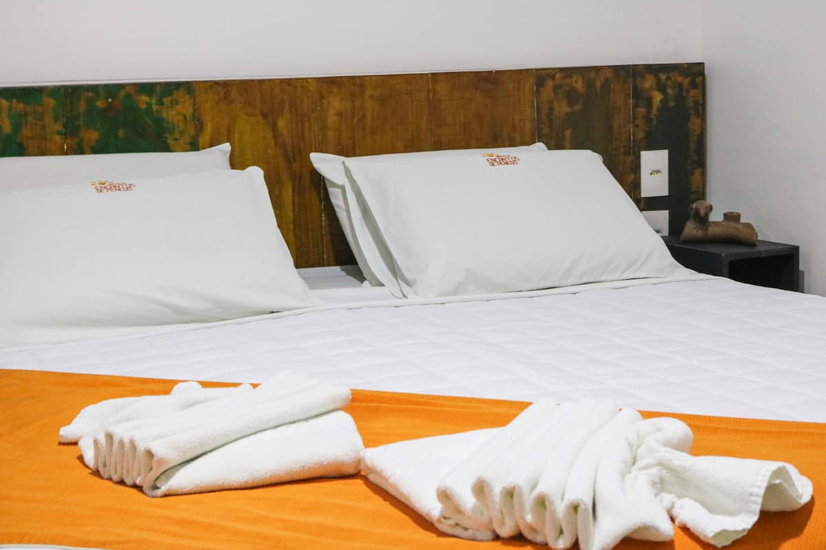 A hotel room with a neatly made bed, two pillows, an orange bedspread, and a folded towel on the bed.