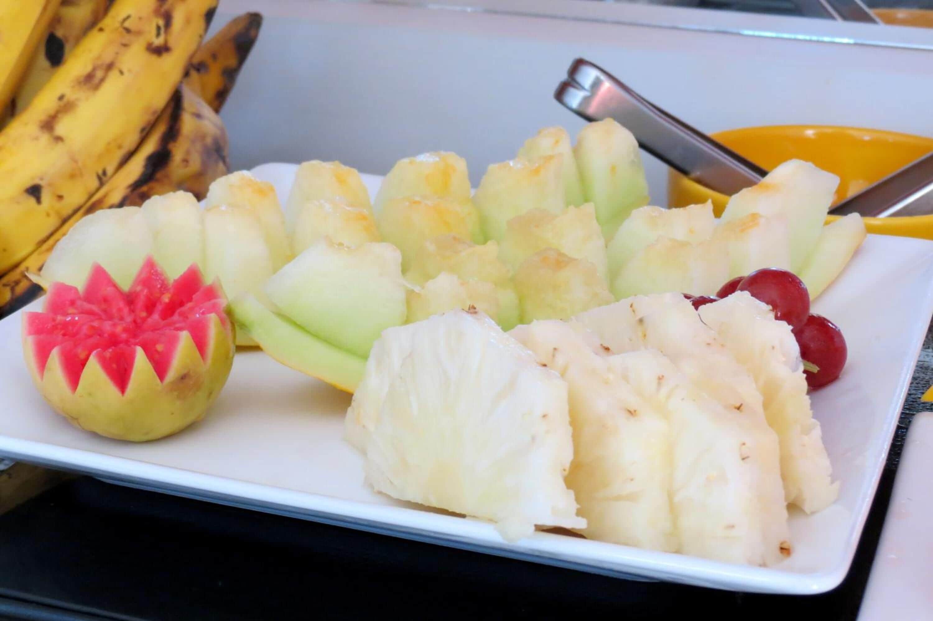 Un plato con frutas cortadas de diferentes maneras, incluyendo sandía, piña y uvas.