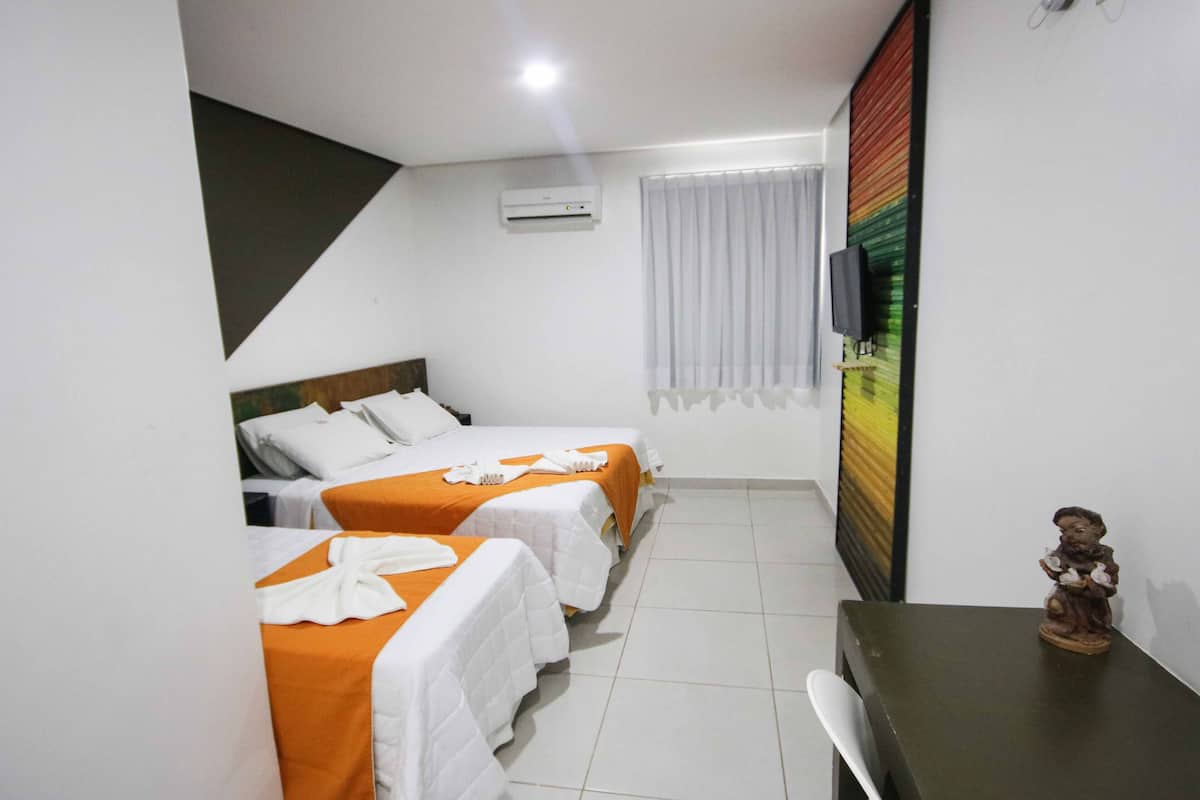 A hotel room with two beds, a small table, a TV, and an air conditioning unit.