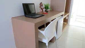 A workspace with a laptop, a small statue, and a potted plant on a brown desk. - Hotel Encantos De Penedo (Penedo)