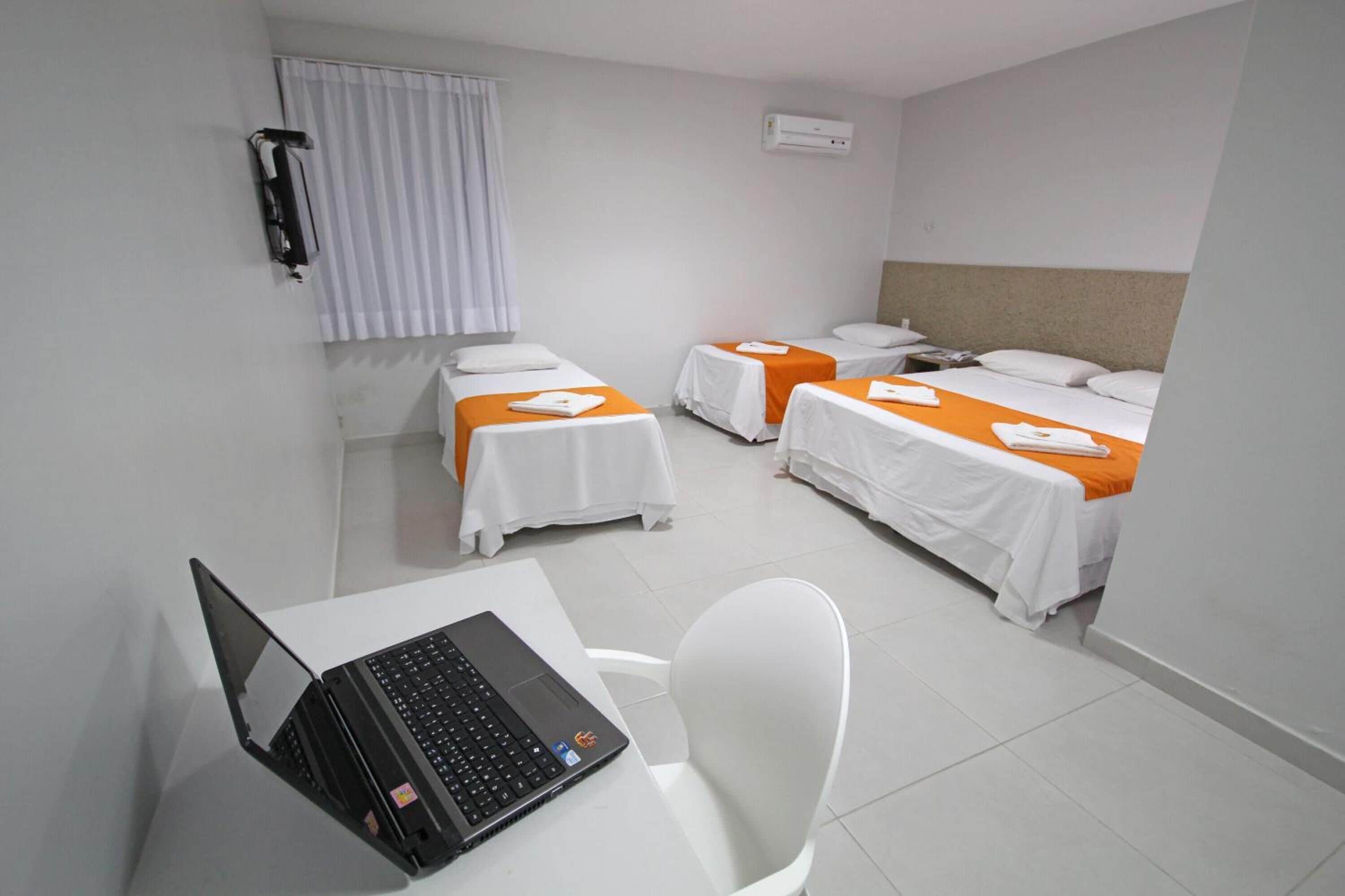 Quarto de hotel com duas camas de solteiro, uma escrivaninha com um laptop e uma cadeira.