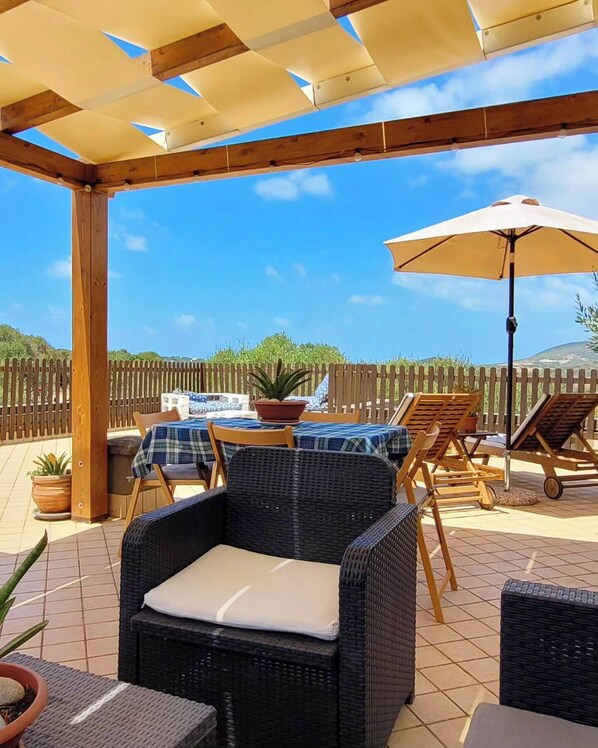 An outdoor patio area with wicker furniture, a table with a checkered tablecloth, and a large umbrella.