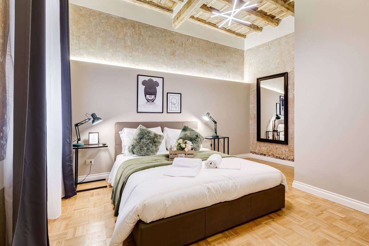 Un dormitorio moderno con una cama grande, suelo de madera y techo con vigas a la vista.