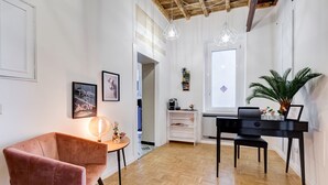 Et moderne værelse med et trægulv i fiskebensmønster, et sort skrivebord, en pink stol og en potteplante.