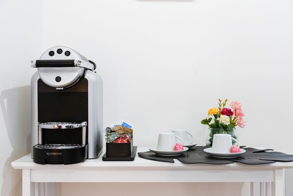 Una cafetera, una pequeña caja de regalo, un florero con flores y una taza blanca sobre una mesa.