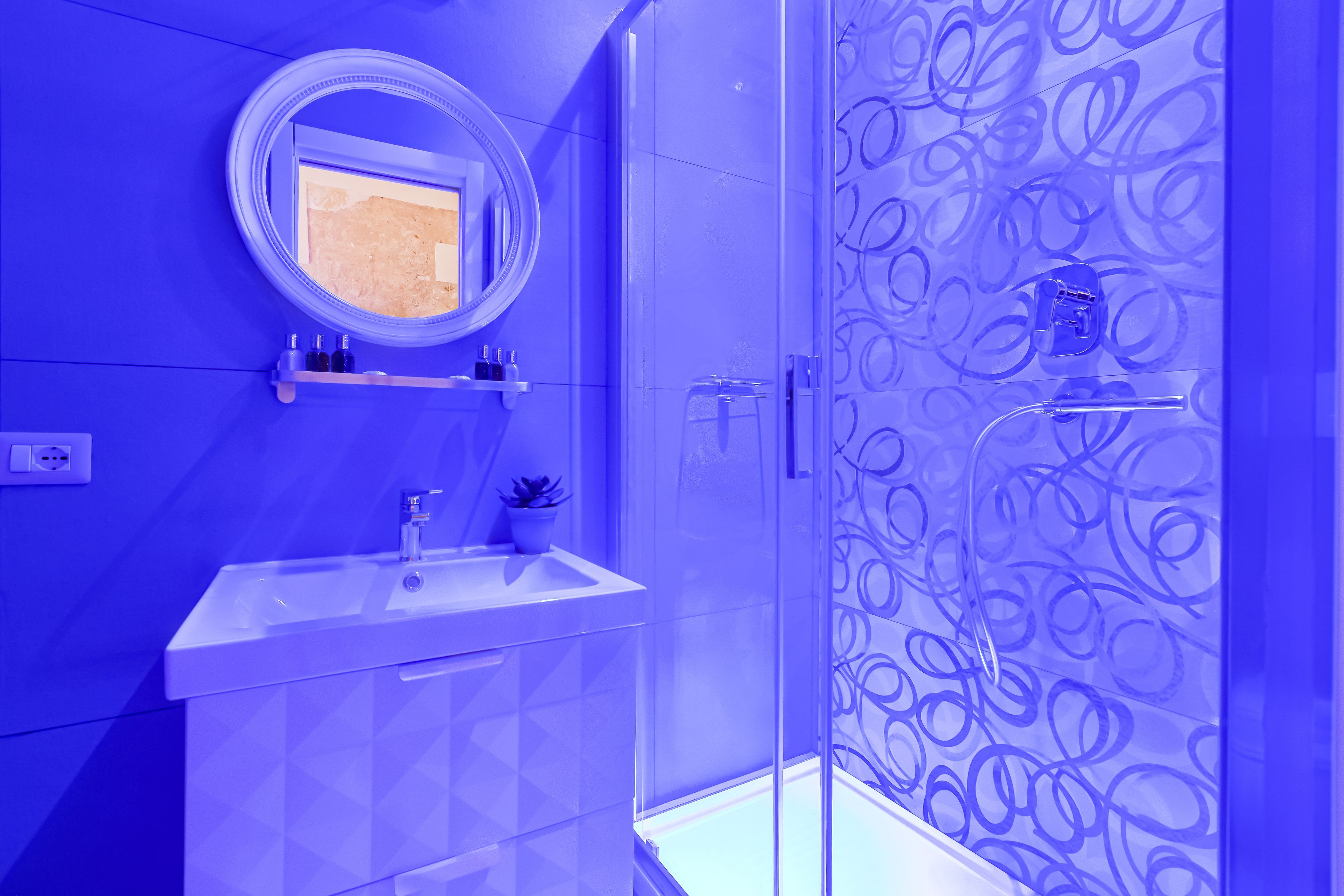 Une salle de bain avec une douche à parois de verre, un lavabo avec un miroir au-dessus et un mur décoré d’un motif.