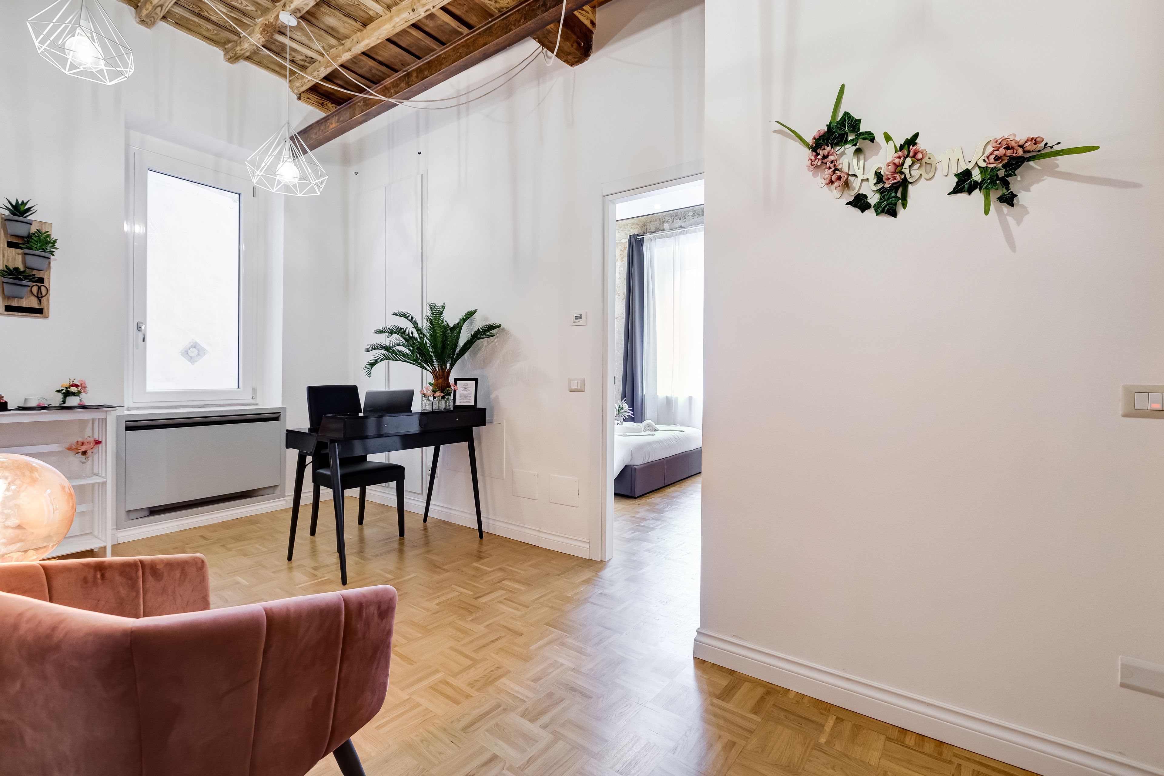 A modern living room with a wooden ceiling, a black dining table, a pink chair, and a potted plant.