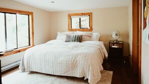 A bedroom with a large bed, a window, a bedside table with a lamp, and a door. - The Perfect Catskills Lake House (Yulan)