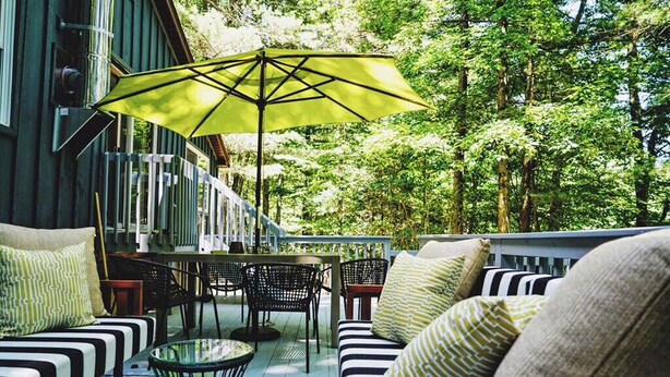 An outdoor seating area with a table, chairs, and a yellow umbrella. - The Perfect Catskills Lake House (Yulan)