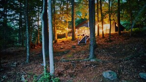 A cabin in a forest with a wooden deck and stairs leading to a porch. - The Perfect Catskills Lake House (Yulan)