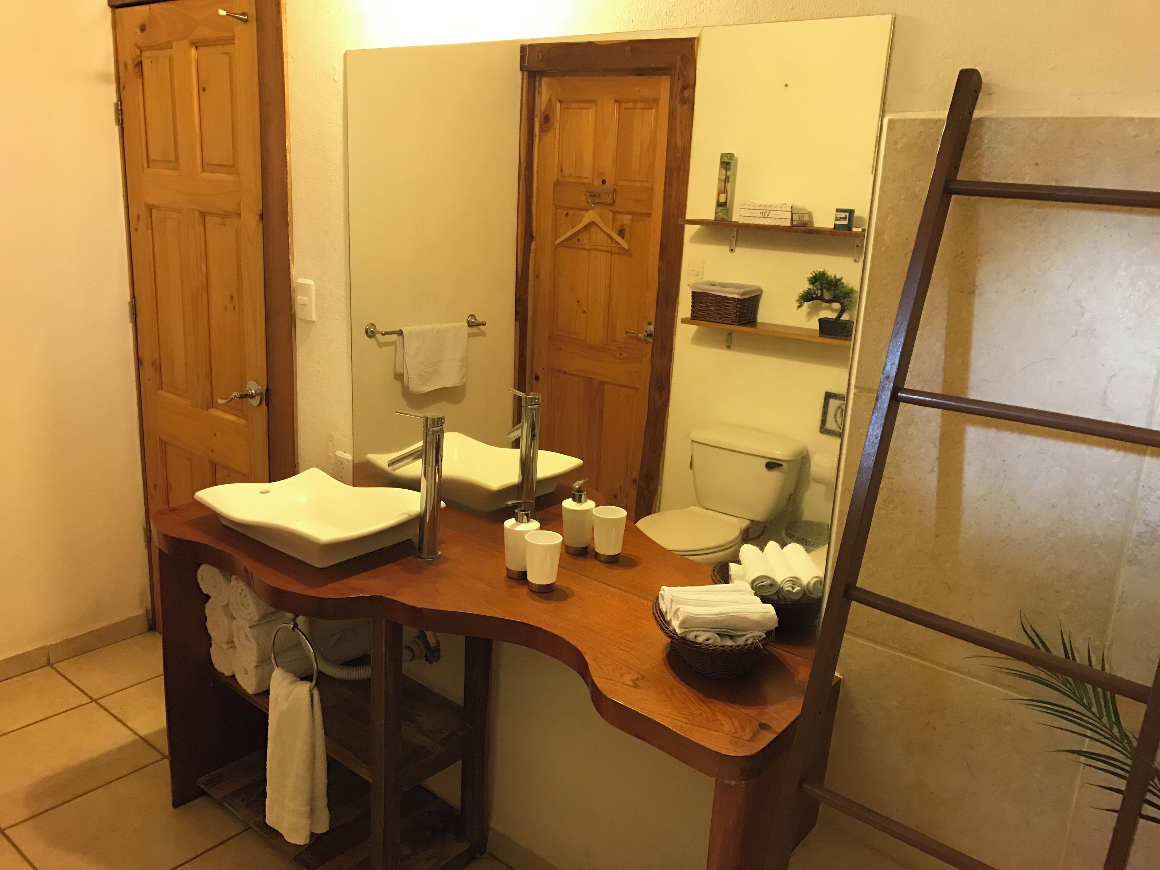 A bathroom with a wooden vanity, two sinks, a toilet, and a towel rack.