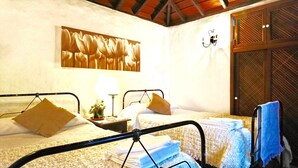 A hotel room with two beds, a nightstand with a lamp, a wall-mounted artwork, and a wooden door.