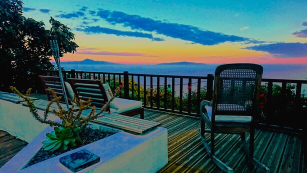 A deck with outdoor seating, a chair, and a view of the mountains at sunset.