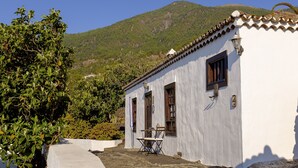 A white building with a tiled roof, two windows, and a small table with chairs outside.