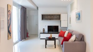 A modern living room with a sofa, a coffee table, a flat-screen TV, and a kitchen area with cabinets and a microwave. - Villa Carlino Holiday (Mascali)