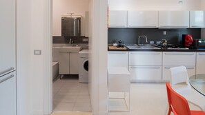 A modern kitchen with white cabinetry, a built-in washing machine, a coffee maker, and a red kettle. - Villa Carlino Holiday (Mascali)