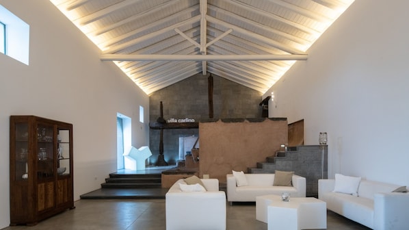 A spacious living area with a high ceiling, white sofas, a wooden cabinet, and a staircase leading to an upper level. - Villa Carlino Holiday (Mascali)