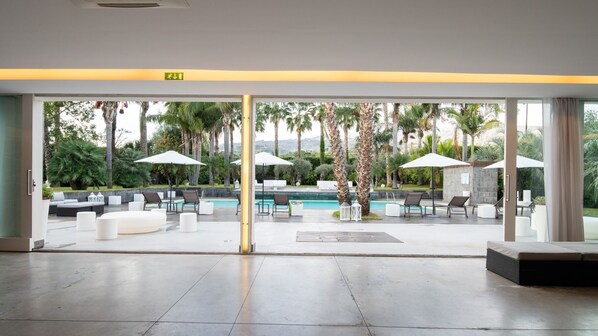 A modern pool area with lounge chairs and umbrellas, a clear view of the pool, and a glass door entrance.