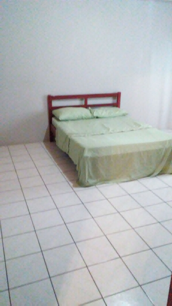 Ein kleines, sauberes Zimmer mit einem Einzelbett, gefliestem Boden in Weiß und schlichten Wänden.
