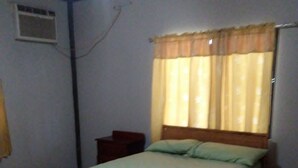 Un lit simple avec un cadre en bois et un matelas vert, dans une pièce dont le sol est recouvert de carreaux.