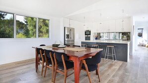 A modern kitchen with white cabinetry, stainless steel appliances, and a central island with bar stools. - Oceanside - Pet Friendly Absolute Beachfront (Culburra Beach)