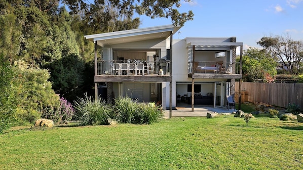 A two-story modern house with a balcony, a garage, and a well-maintained garden. - Oceanside - Pet Friendly Absolute Beachfront (Culburra Beach)