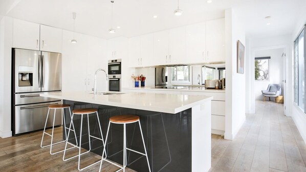 A modern kitchen with a large island, stainless steel appliances, and bar stools. - Oceanside - Pet Friendly Absolute Beachfront (Culburra Beach)