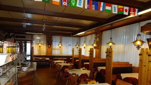 A restaurant with wooden benches and tables, a bar area with bottles, and flags hanging from the ceiling. - Hotel Calalzo (Calalzo di Cadore)