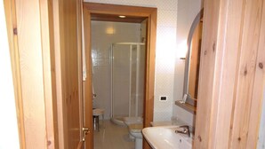 A narrow bathroom with a wooden door, a white sink, a toilet, and a shower stall. - Hotel Calalzo (Calalzo di Cadore)