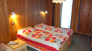 A double bed with floral bedding, a bedside table with a phone, and a lamp. - Hotel Calalzo (Calalzo di Cadore)