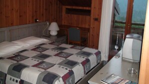 A room with a wooden ceiling and walls, a bed with a quilt, a bedside table with a lamp, and a view of the outdoors through a glass door. - Hotel Calalzo (Calalzo di Cadore)
