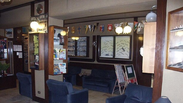 A lobby with blue armchairs, a coffee table, a map on the wall, and a bulletin board with various notices. - Hotel Calalzo (Calalzo di Cadore)