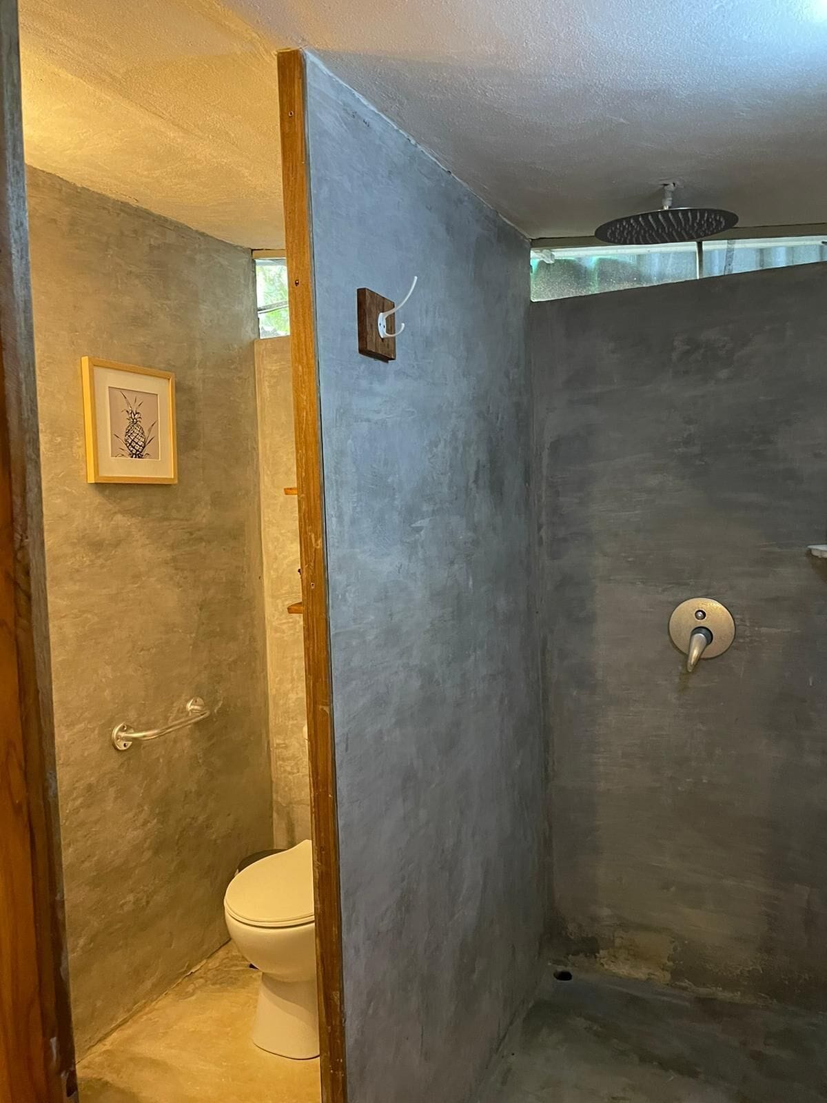 A bathroom with a toilet, a shower with a control knob, and a framed picture on the wall.