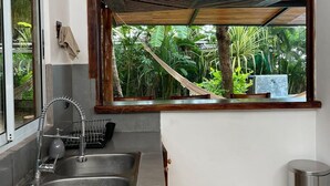 Una cocina con lavaplatos integrado, ventana con vistas a un jardín y un cesto de basura.