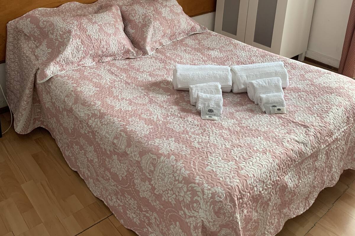 Una cama bien hecha con una colcha y almohadas de estampado floral, un cabecero de madera y un armario blanco con rayas verticales.