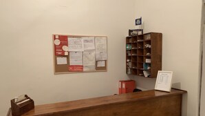 Een receptiebalie met een prikbord, een houten plank met diverse objecten, en een lijst met een bord.'