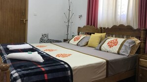 A double bed with a wooden headboard, a bedside table, a nightstand, a mirror, a window with curtains, and a door. - Mulberry Homestay  . (Thekkady)