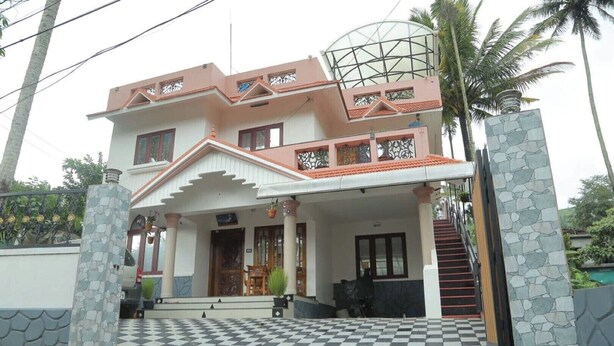 A two-story house with a checkered driveway, a porch with columns, and a staircase leading to the entrance. - Mulberry Homestay  . (Thekkady)