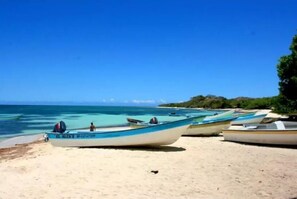 Une plage où plusieurs bateaux sont alignés sur le sable, un ciel bleu clair et une mer calme.