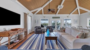 A spacious living room with a high ceiling, a ceiling fan, and a large window overlooking a deck. - Tailwind South: Beautiful 3 bedroom across the street from Beach! (Placida)