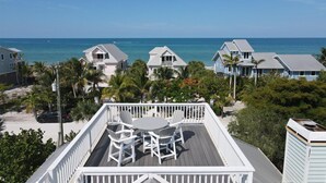 A deck with a table and chairs overlooking a beach with houses and the ocean. - Tailwind South: Beautiful 3 bedroom across the street from Beach! (Placida)
